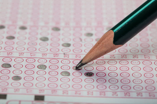 istock high school or university student hands taking exams, writing examination on paper answer sheet optical form of standardized test on desk doing final exam in classroom. Education literacy concept. 1138253452