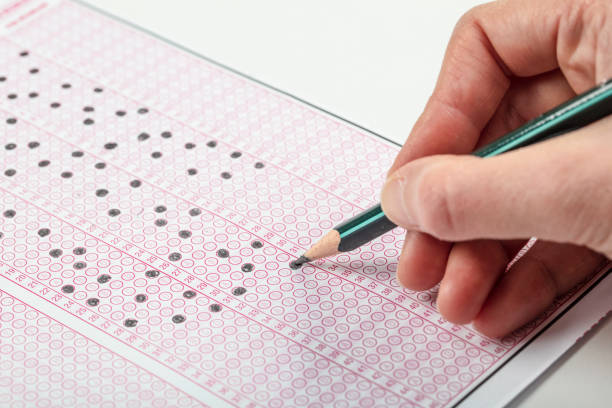 istock high school or university student hands taking exams, writing examination on paper answer sheet optical form of standardized test on desk doing final exam in classroom. Education literacy concept. 1138253599