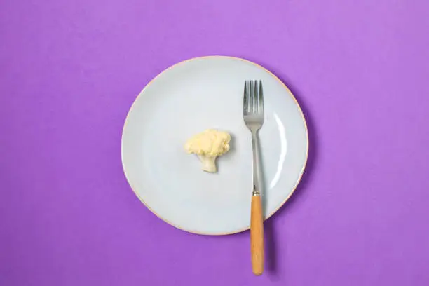 Diet, weight loss minimal concept, healthy eating - cauliflower on plate, top view, copy space, purple background