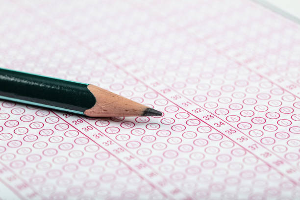 high school or university student hands taking exams, writing examination on paper answer sheet optical form of standardized test on desk doing final exam in classroom. Education literacy concept.