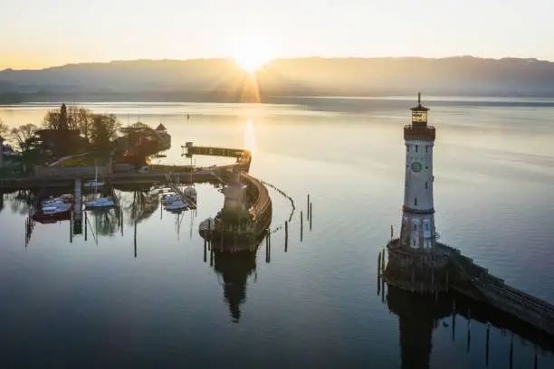 Sunrise over Bodensee Harbor Entrance of Lindau with the famous Lighthouse and Bavarian Lion Sculpture (from the year 1856). Sunrise, Aerial Drone point of View. Lindau, Bodensee, Bavaria, Germany.