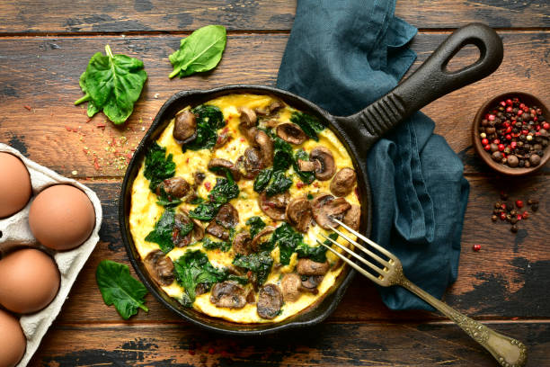 Omelette with mushrooms and spinach in a cast iron pan Omelette with mushrooms and spinach in a cast iron pan on a dark rustic wooden background.Top view with copy space. omelet rustic food food and drink stock pictures, royalty-free photos & images