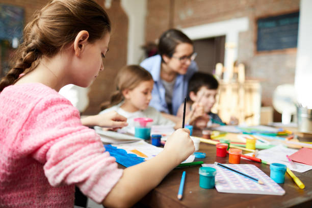 Back View of Girl Painting in Art Class Back view portrait of teenage girl painting picture in art class with group of children, copy space young children pictures stock pictures, royalty-free photos & images