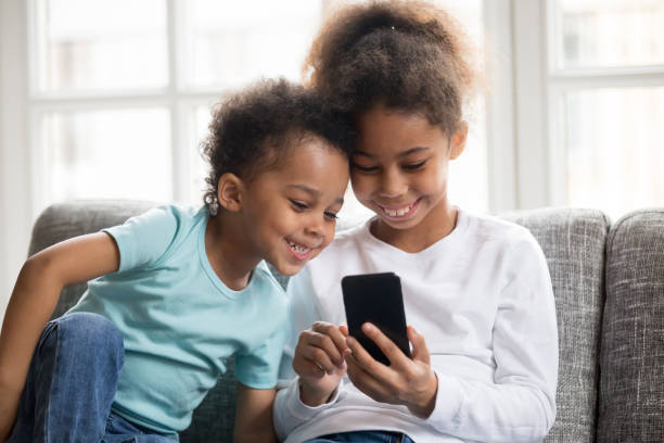 smiling little black kids play with smartphone together - african ethnicity brother ethnic little boys imagens e fotografias de stock