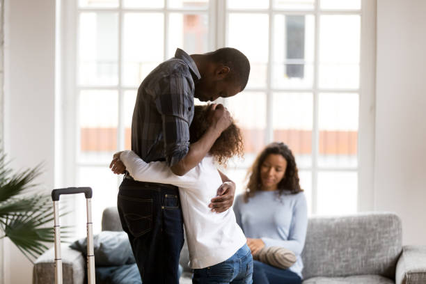 Sad African American girl hug dad leaving home with suitcase Cute sad little African American girl hug dad standing with suitcase leaving for business trip, upset small mixed race kid embrace father saying goodbye, parents separating. Shared custody concept divorce stock pictures, royalty-free photos & images
