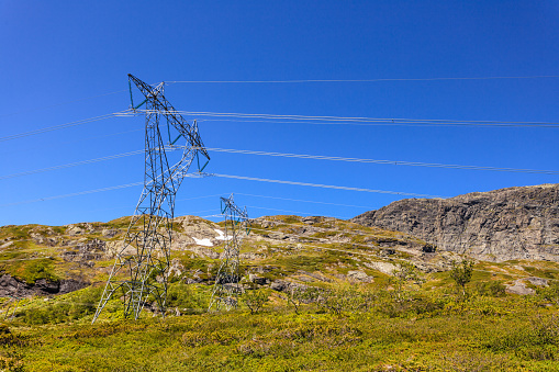 Electricity transmission pylons, power lines high voltage towers in norwegian mountains landscape.