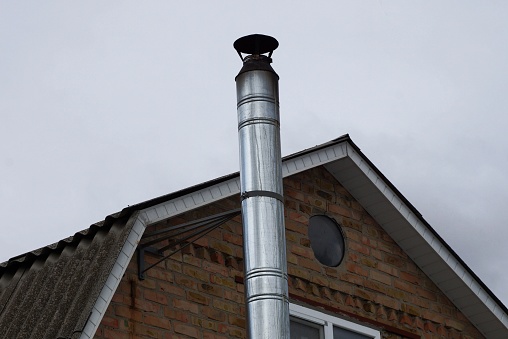 one gray long metal pipe chimney on a brown brick loft against the sky