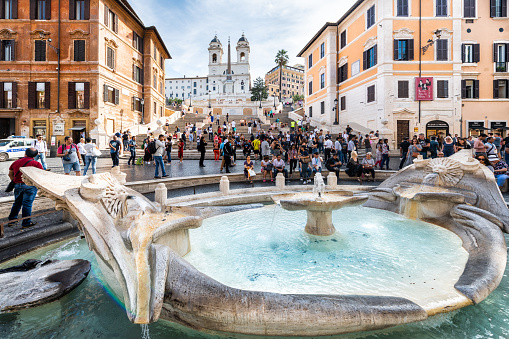 Rome, Italy - September 4, 2018: Historic city with famous Spanish Steps on summer day closeup of water fountain and many crowd of people tourists sightseeing