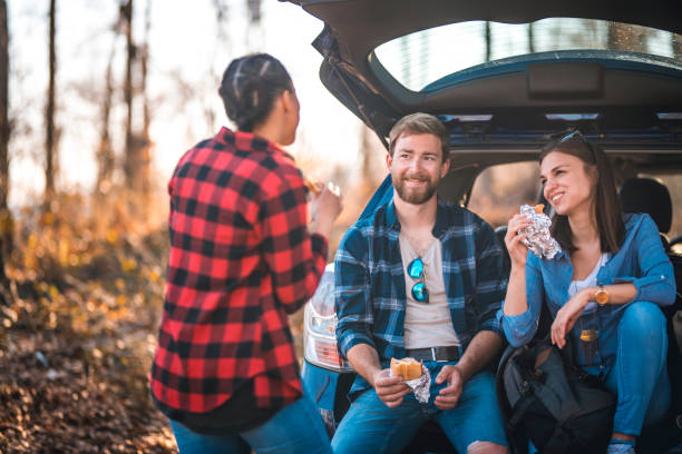 friends talking next to a car trunk in forest and having sandwiches - 1474 imagens e fotografias de stock