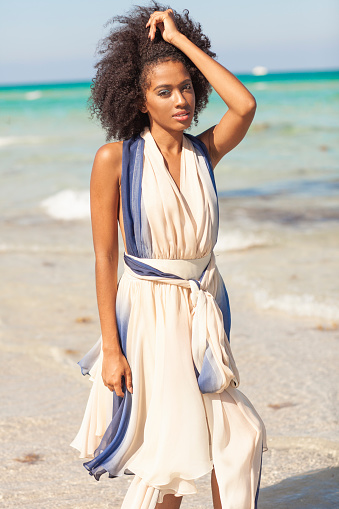 Beautiful woman with afro hair walking at the beach wearing tulle dress.