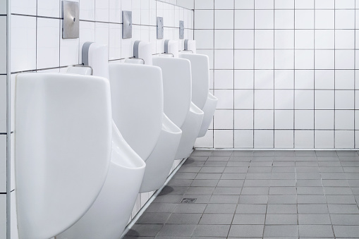 row of white urinals in men's public bathroom toilet with white tiles wall.