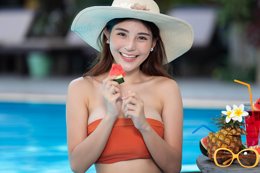 Beautiful female in bikini relaxing at the pool holding watermelon with cocktail.
