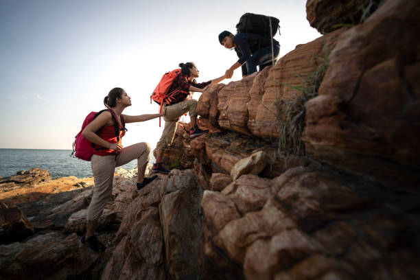 アジアハイキングのグループは、太陽の光で山のシルエットをお互いに助けます。 - people traveling journey group of people hiking ストックフォトと画像