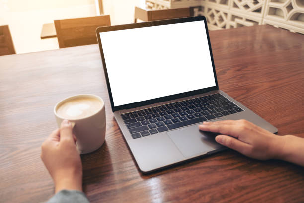 istock Mockup image of a woman using and touching on laptop touchpad with blank white desktop screen on wooden table while drinking coffee 1138301209