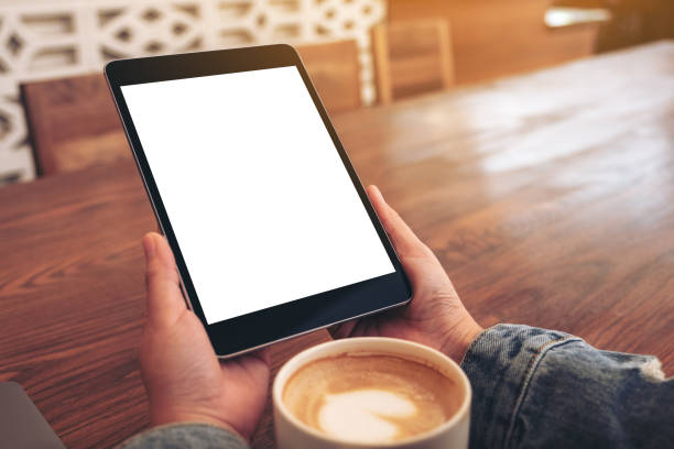 istock Mockup image of hands holding black tablet pc with blank white screen with coffee cup on wooden table 1138301258