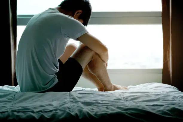 Photo of Young man sitting on the bed are unhappy and stressed at the windows of the room.