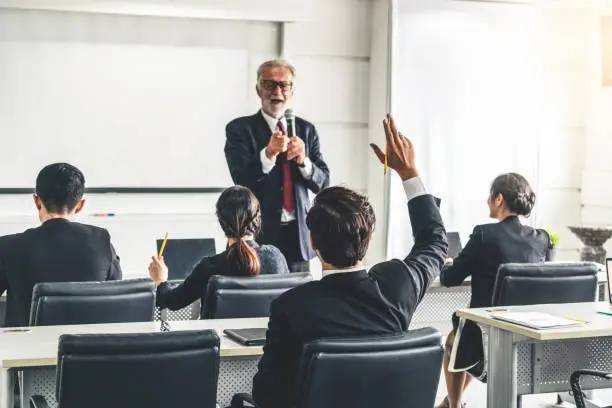 Photo of Senior leader speaker speaks to public people audience in training workshop or conference. Mature lecturer is CEO executive manager leading the symposium event. International business seminar concept.