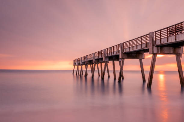 Pier with sun behind clouds at sunrise