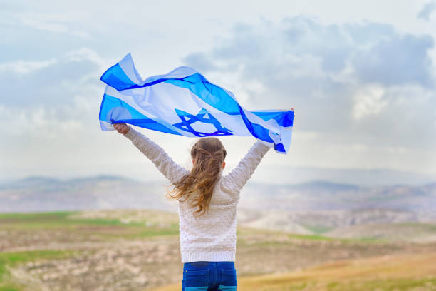 pequeña chica judía patriota de pie y disfrutando con la bandera de israel en el cielo azul de fondo. memorial day-yom hazikaron, festividad patriótica día de la independencia israel-yom ha'atzmaut concept - israel fotografías e imágenes de stock