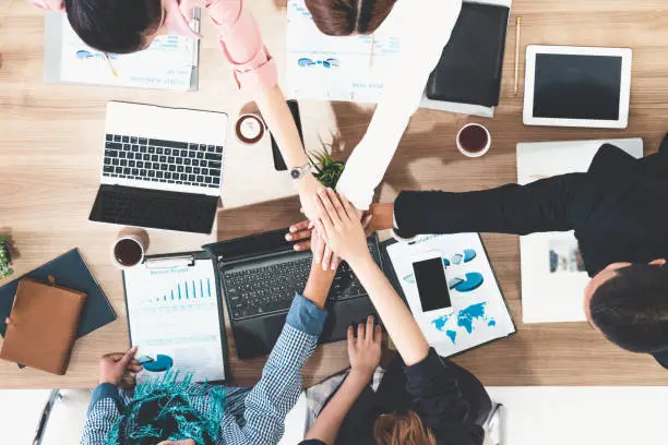 Photo of Businessmen and businesswomen joining hands in group meeting at multicultural office room showing teamwork, support and unity in business. Diversity workplace and corporate people working concept.