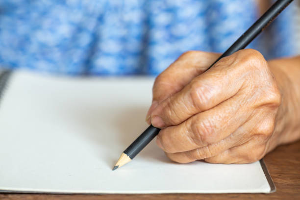 istock Senior woman's left Hand writing letter on ivory paper background, Notebook, A black pencil, Close up & Macro shot, Selective focus, Stationery concept 1138314655