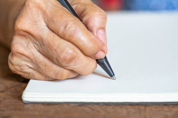 istock Senior woman's right Hand writing letter on ivory paper background, Notebook, A black pen, Close up & Macro shot, Selective focus, Stationery concept 1138314698