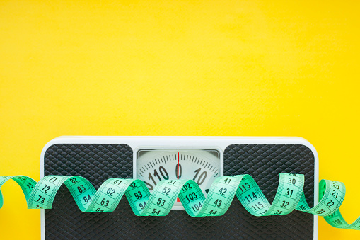 Fruits, measuring tape and weighing-machine on the yellow background.
Weight loss, diet control and healthy food concept background.