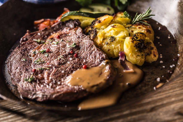 ジューシービーフリブアイステーキローストポテトソース添え野菜の塩コショウとハーブのヴィンテージパン - rib eye steak steak beef prepared potato ストックフォトと画像