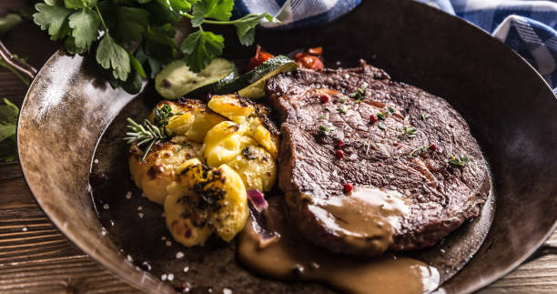 ジューシービーフリブアイステーキローストポテトソース添え野菜の塩コショウとハーブのヴィンテージパン - rib eye steak steak beef prepared potato ストックフォトと画像