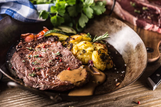 ジューシービーフリブアイステーキローストポテトソース添え野菜の塩コショウとハーブのヴィンテージパン - rib eye steak steak beef prepared potato ストックフォトと画像