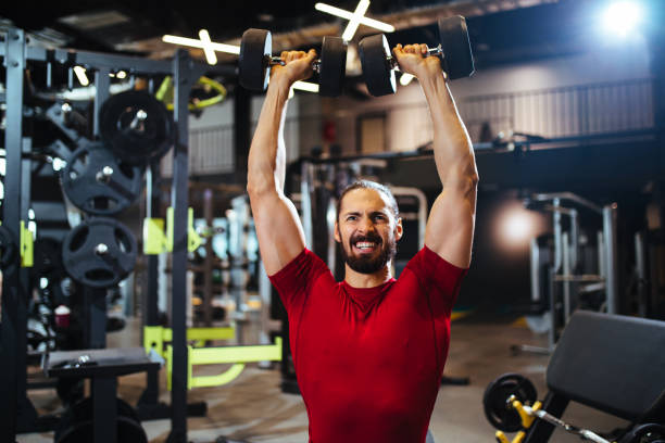 istock Young man lifting up dumbbells at the gym 1138341831