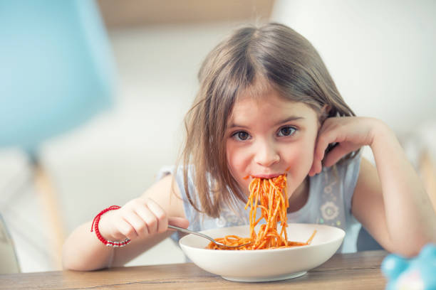 linda niña pequeña comiendo espaguetis a la boloñesa en casa. - espagueti fotos fotografías e imágenes de stock