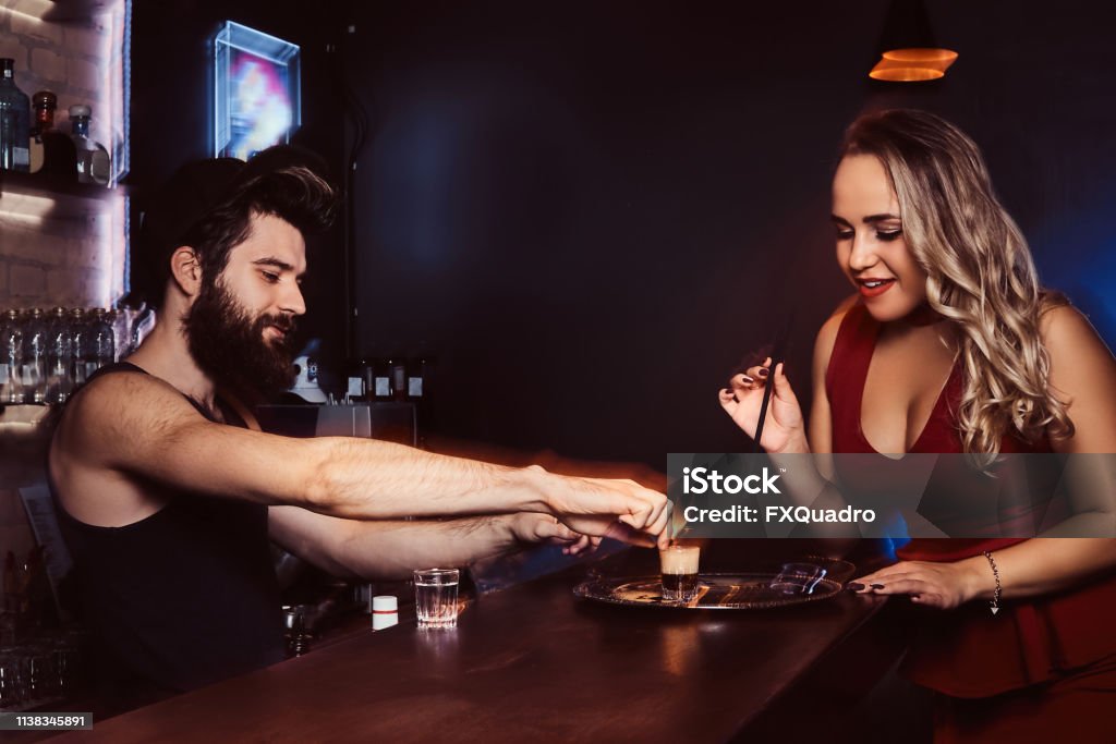 A beautiful girl in a red dress is holding a straw and waiting for the barman to make a cocktail A beautiful girl in a red dress is holding a straw and waiting for the barman to make a cocktail at the bar. Cocktail Stock Photo