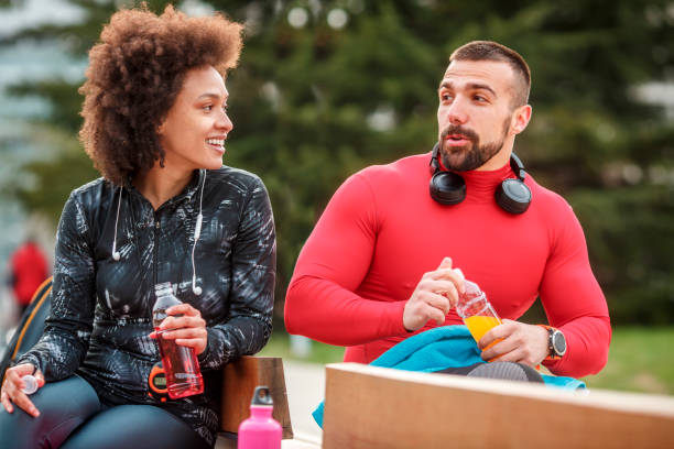 istock Young athletic couple sitting next to each other on a bench in a park and talking while hydrating themselves with bottled energy drinks 1138348170