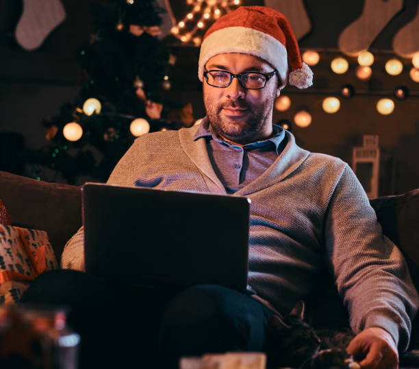 istock Happy man in glasses stroking a cat and using laptop while sitting on sofa at Christmas time. 1138353108
