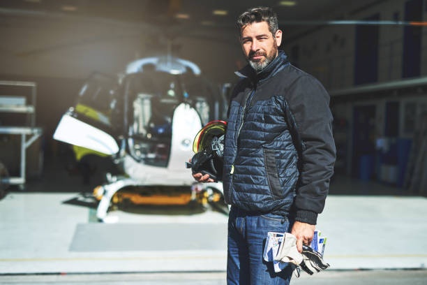 Are you coming eith me? Shot of a cheerful middle aged man ready to pilot an helicopter that is placed in the background inside of a hangar helicopter modern stock pictures, royalty-free photos & images