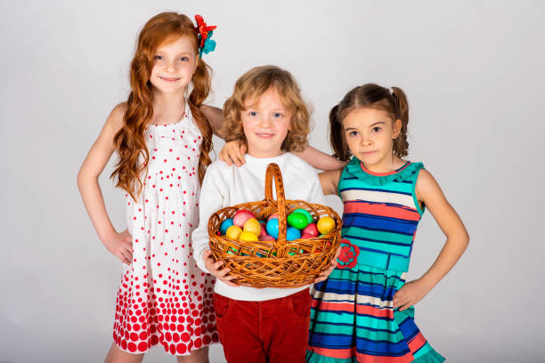 Three lovely children on a white background, the boy is holding a basket with Easter eggs, and the girls are on the sides