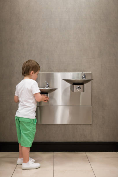Curious kid boy drinking water from drinking fountain. Stainless Steel drinking fountains mounted at different heights. Young customer in the shop. Curious kid boy drinking water from drinking fountain. Stainless Steel drinking fountains mounted at different heights. Young customer in the shop. whites only drinking fountain stock pictures, royalty-free photos & images