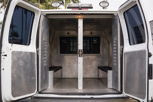 Rear view of a police van for the transportation of prisoners parked near the police station. Inside a police car. Open doors of a police van.