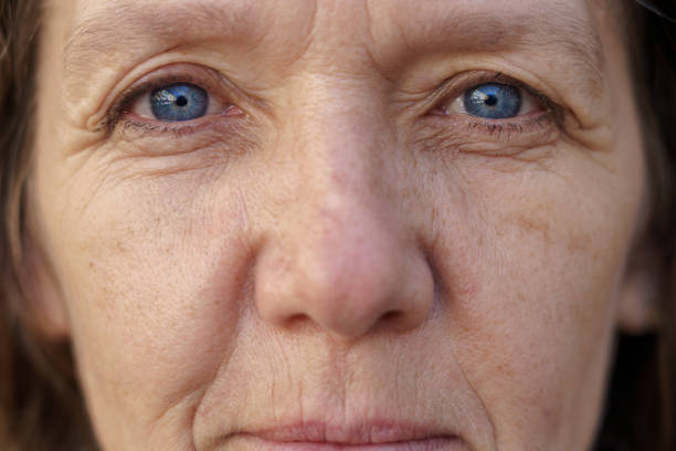 Cropped face of a blue-eyed middle-aged woman Cropped face of a blue-eyed middle-aged woman with wrinkled skin looking into the lens in a concept of ageing smokers wrinkles stock pictures, royalty-free photos & images