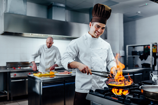 Team of Latin American chefs cooking together and sautéing some vegetables in a pan while smiling - preparing food concepts