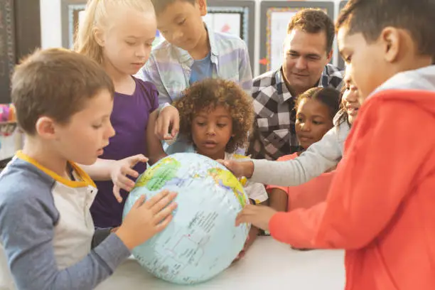 Front view of a schoolteacher discusing over a earth globe in classroom at school with his school kids