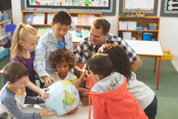 istock Schoolteacher interacting with his pupils over a earth globe putting on a table in classroom at scho 1138358591