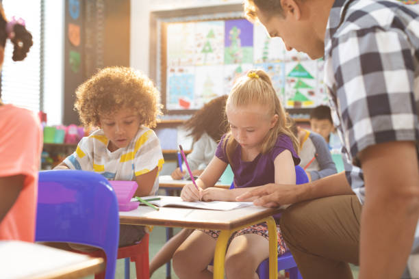 istock Teacher interacting with school girl while sitting in classroom 1138358629