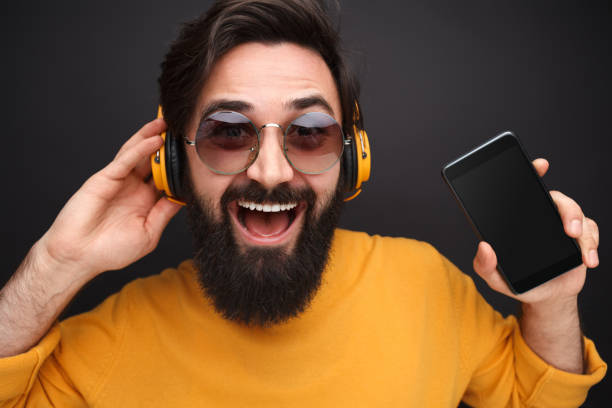 istock Cheerful guy in headphones showing smartphone 1138358778