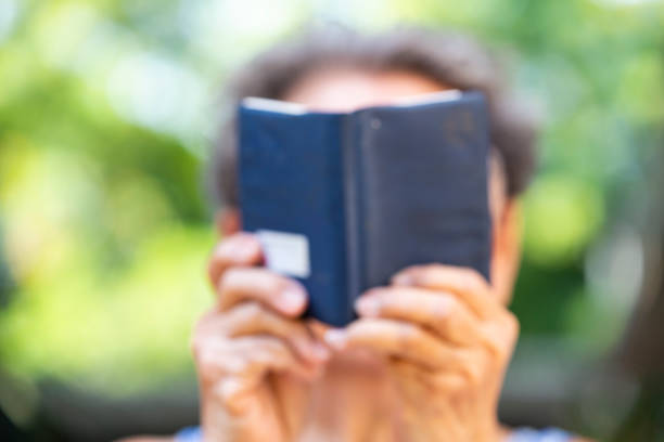 donna senior sfocata che legge un piccolo libro di colori blu navy sullo sfondo del giardino bokeh, primo piano & macro scatto, messa a fuoco selettiva, tempo di relax - arts symbols studio shot selective focus entertainment foto e immagini stock