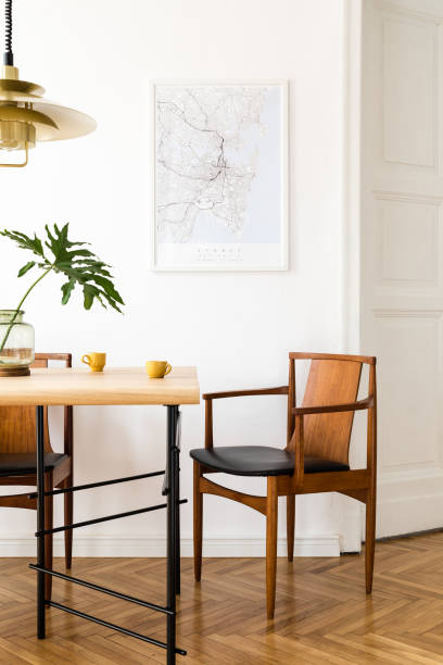 Stylish and modern dining room interior with mock up poster map, sharing table design chairs, gold pedant lamp and cups of coffee. White walls, wooden parquet. Tropical leafs in vase. Eclectic decor. Stylish and modern dining room interior with mock up poster. Eclectic decor. wooden bleachers stock pictures, royalty-free photos & images