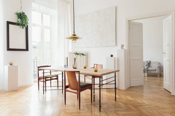 istock Eclectic and elegant dining room interior with design sharing table, chairs, gold pedant lamp, abstract paintings and stylish accessories. View to living room. Minimalist decor. Brown wooden parquet. 1138361045