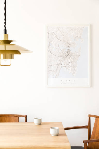 istock Stylish and modern dining room interior with mock up poster map, sharing table design chairs, gold pedant lamp and cups of coffee. White walls, wooden parquet. Minimalistic and eclectic decor. 1138361084