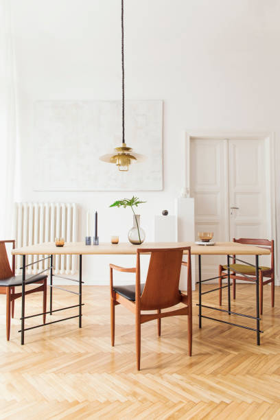 istock Eclectic and elegant dining room interior with design sharing table, chairs, gold pedant lamp, abstract paintings and stylish accessories.Tropical leafs in vase. Minimalistic decor. Real photo. 1138361102